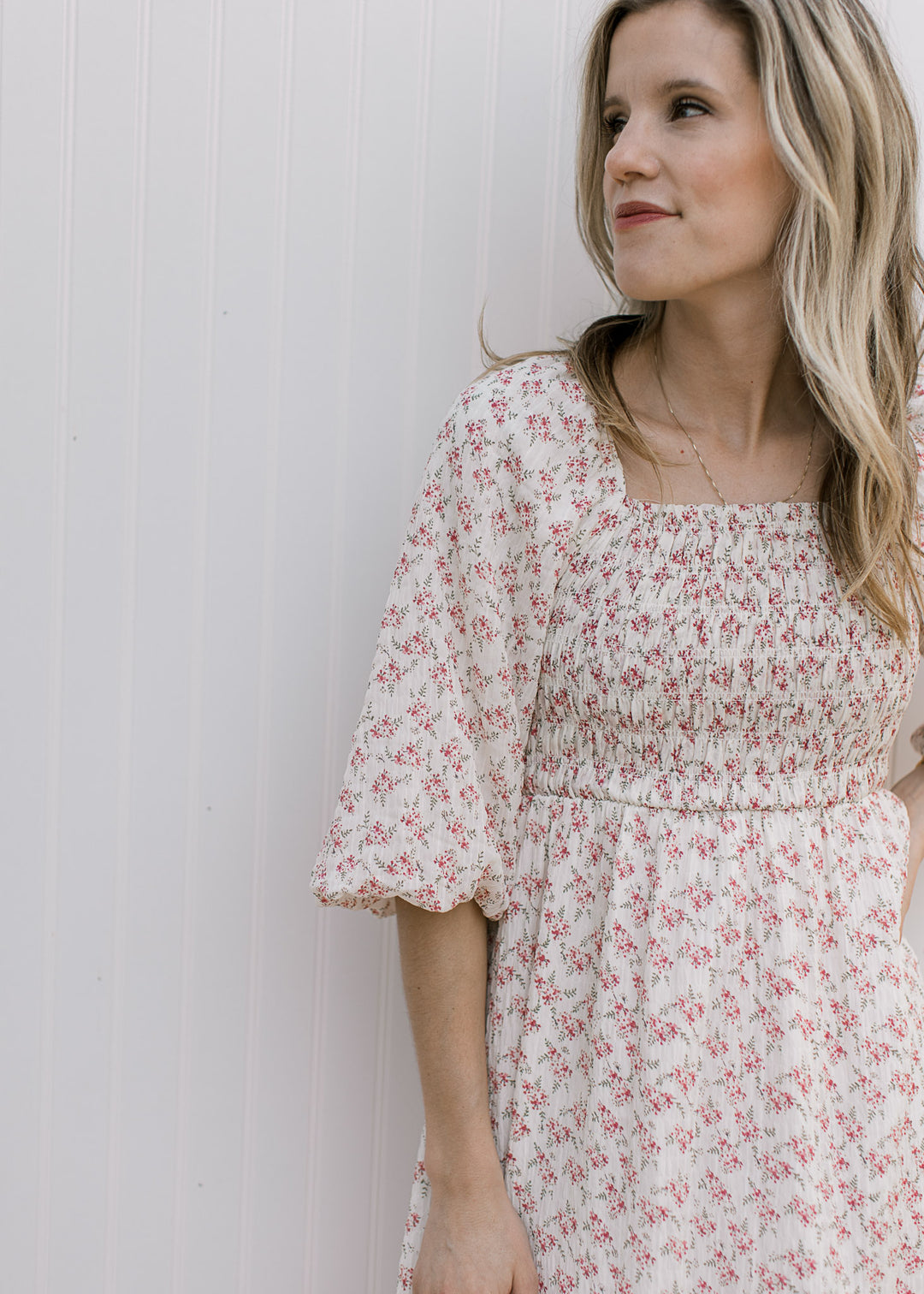 Model wearing a cream above the knee dress with rose ditsy floral and a smocked bodice. 