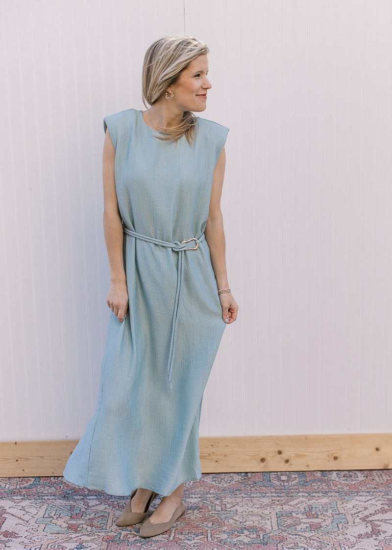 Model wearing a fully lined, sleeveless seafoam dress with a tie belt and shoulder pads. 