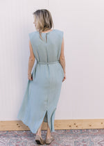 Back view of Model wearing a sleeveless seafoam dress with a tie belt, keyhole closure and split. 