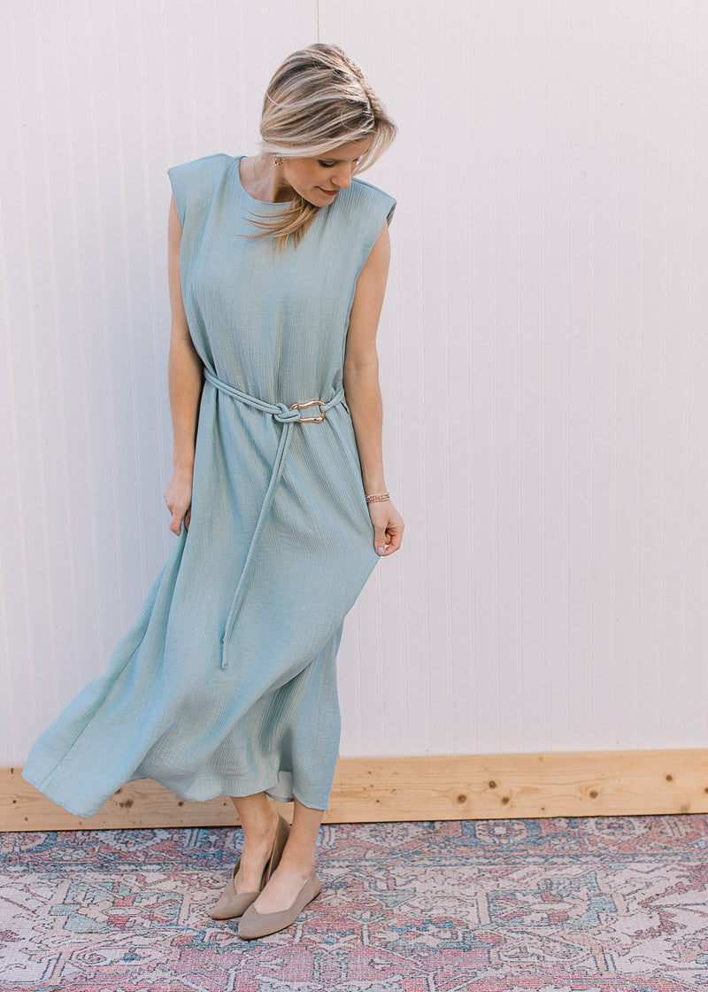 Model wearing a sleeveless seafoam dress with a tie belt, long line fit and shoulder pads. 