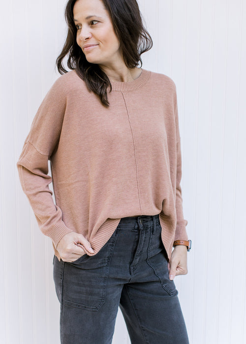 Model wearing a camel colored sweater with a front hem detail, long sleeves and ribbed detail. 