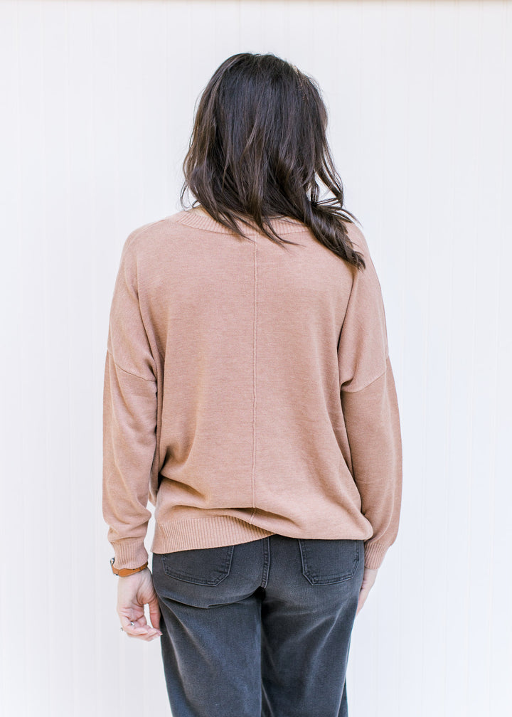 Back view of Model wearing a camel colored sweater with a front hem detail and long sleeves. 