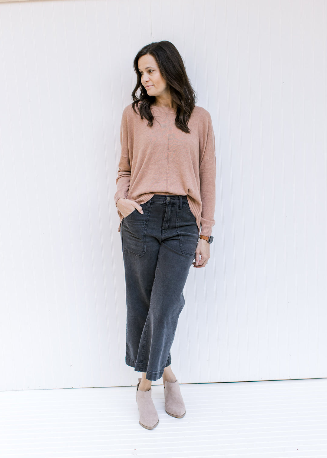 Model wearing jeans and booties with a camel sweater with a front hem detail and long sleeves.