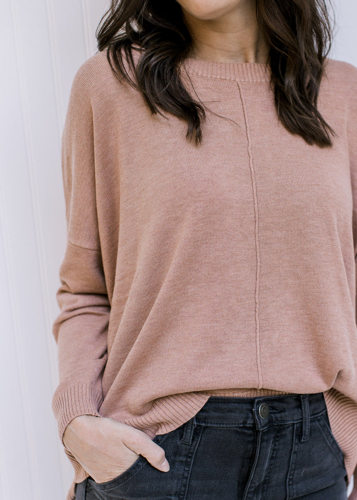 Model wearing a camel colored sweater with a front hem detail, long sleeves and a round neck.