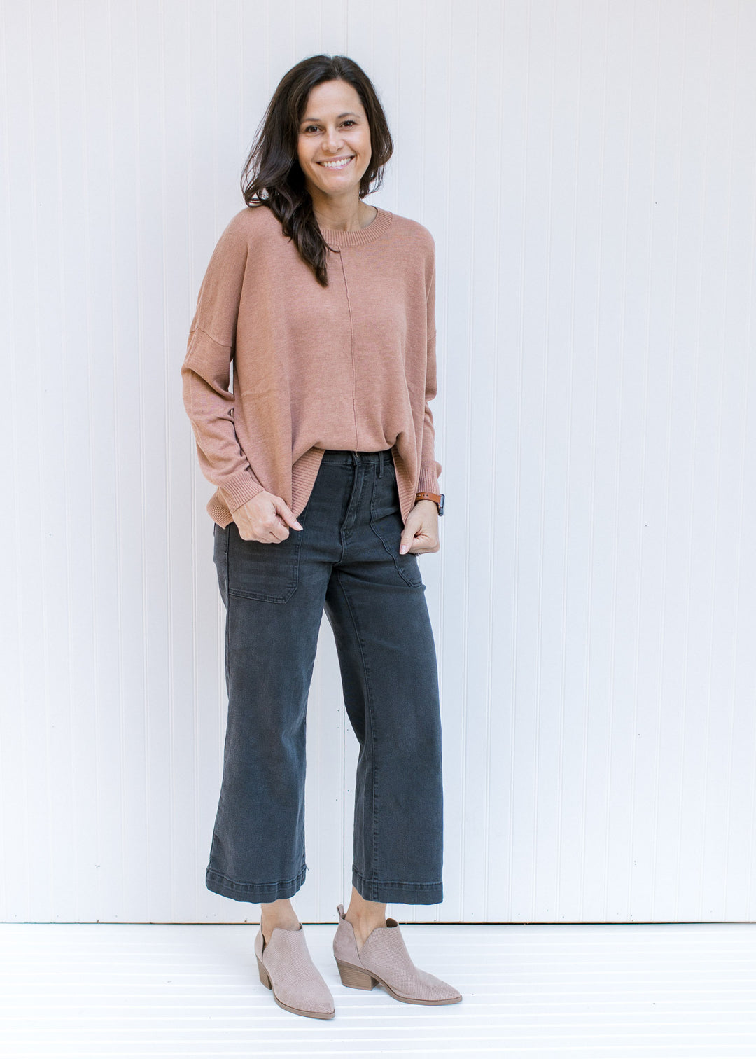 Model wearing jeans with a camel sweater with a front hem detail, long sleeves and a round neck.