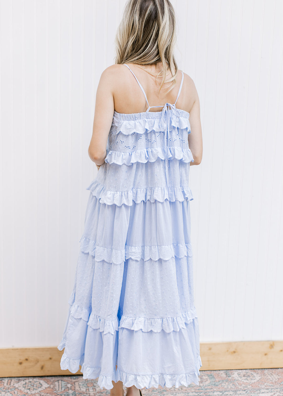 Back view of Model wearing a pale blue midi with ruffle tiers and spaghetti straps with a tie back. 