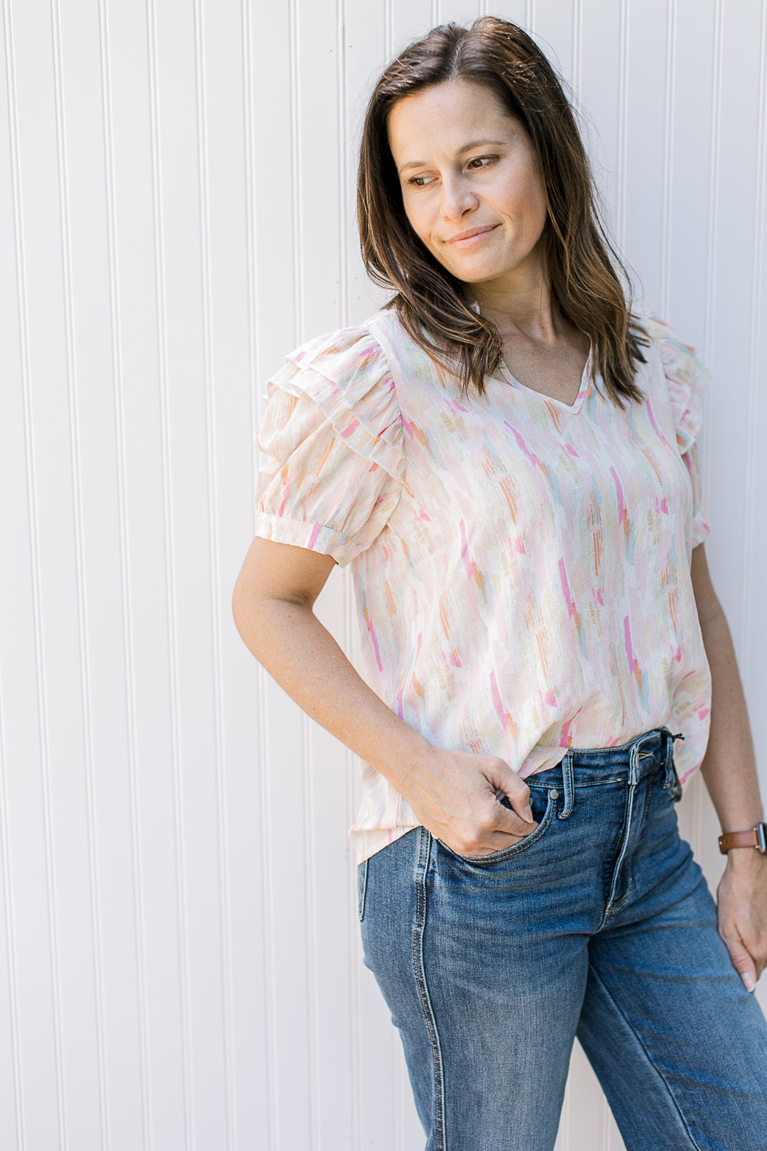 Model wearing jeans with an abstract v-neck top with short puff sleeves and a v-neck.