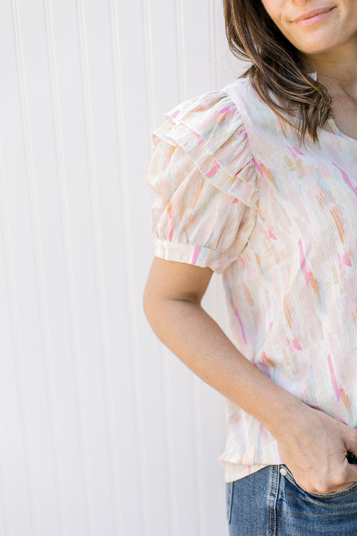 Close up of puff short sleeve with layered ruffle at shoulder on an abstract v-neck top.