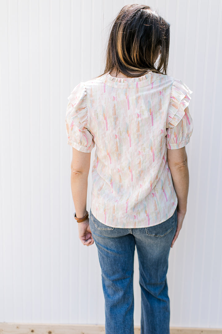 Back view of Model wearing an abstract v-neck top with short puff sleeves and a v-neck.