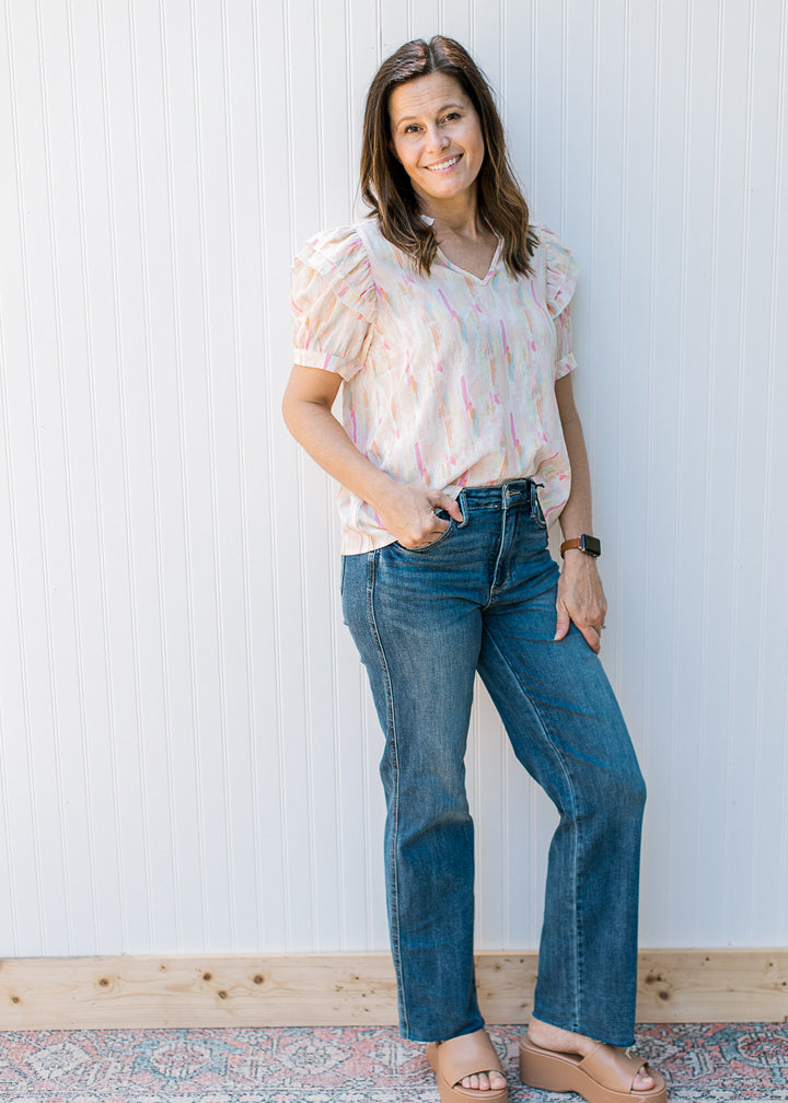 Model wearing jeans and wedges with an abstract v-neck top with short puff sleeves.