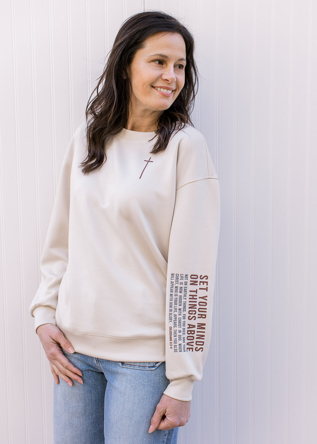 Model wearing a cream pullover with maroon cross round neckline and long sleeves. 
