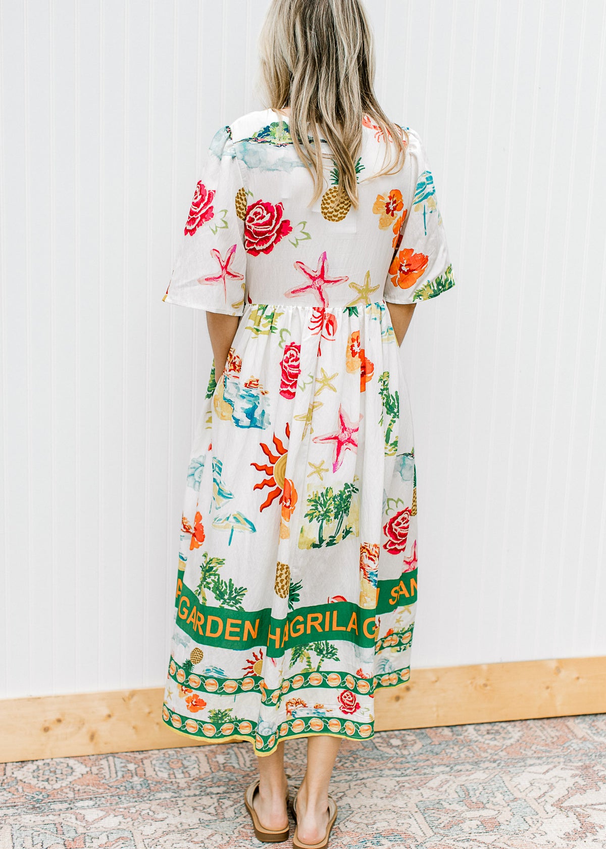 Back view of Model wearing a button up cream midi with av-neck and multicolored tropical pattern. 