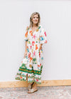 Model wearing sandals and a button up cream midi with a v-neck and multicolored tropical pattern. 