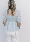 Back view of a pale blue peplum top with a smocked bodice and short sleeves with elastic band.