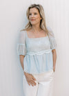 Model wearing a pale blue peplum top with a lace overlay at bodice and a square neck. 