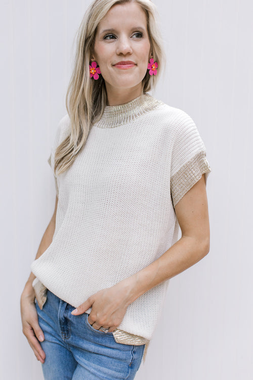 Model wearing a cream cable knit top with gold shimmer at neck, cuff and hem. 
