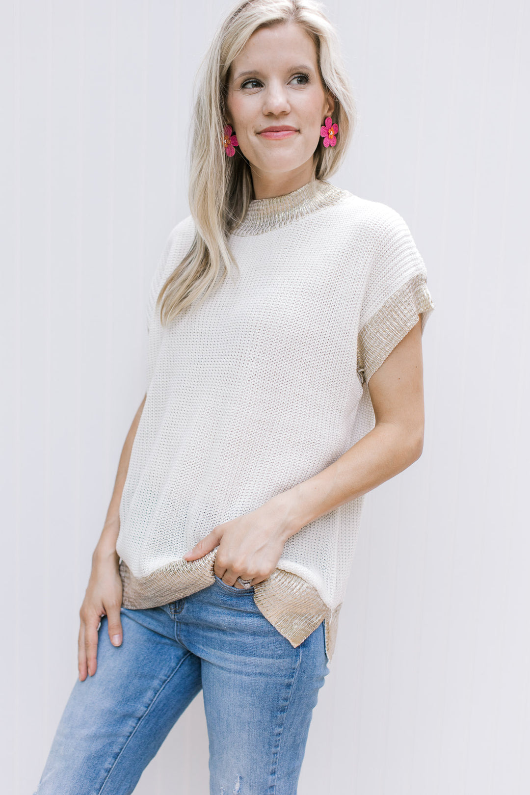 Model wearing pink earrings with a cream cable knit top with gold shimmer at neck, cuff and hem.