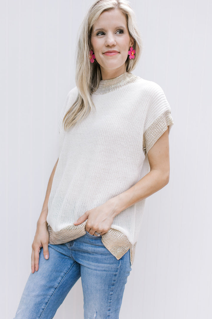 Model wearing pink earrings with a cream cable knit top with gold shimmer at neck, cuff and hem.
