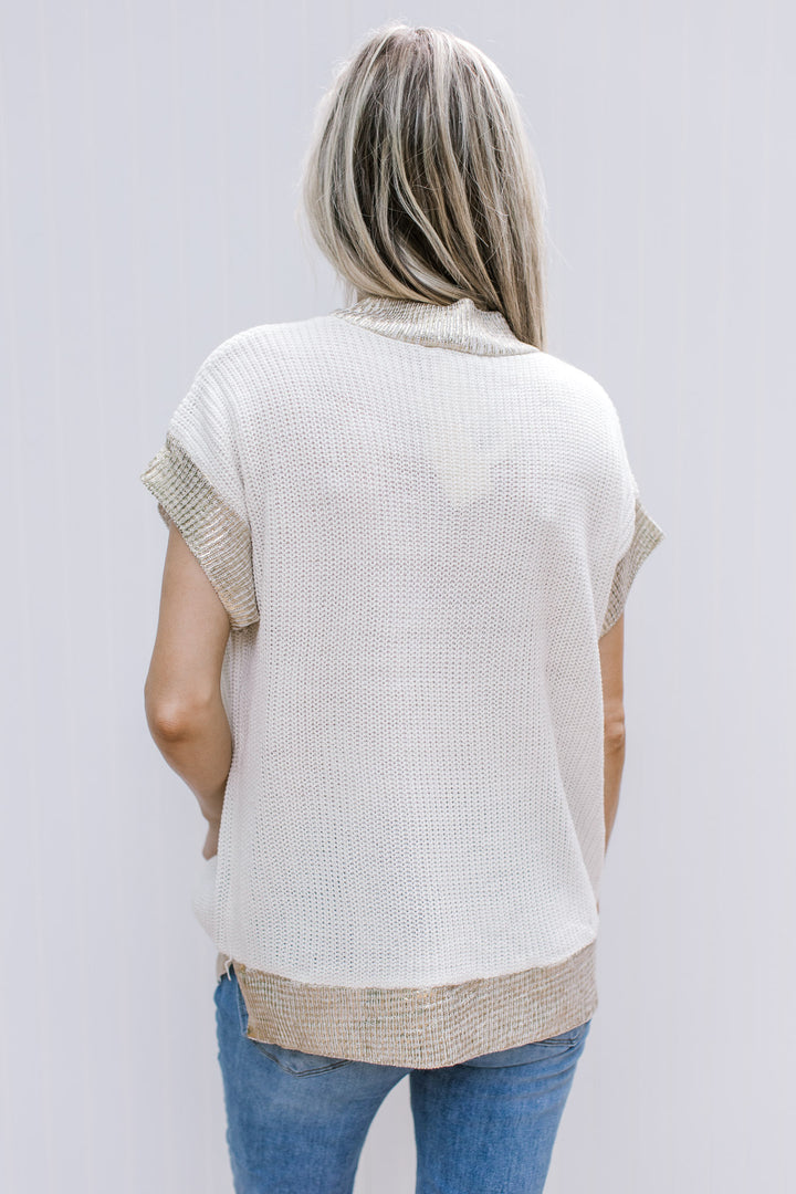 Back view of Model wearing a cream cable knit top with gold shimmer at neck, cuff and hem.