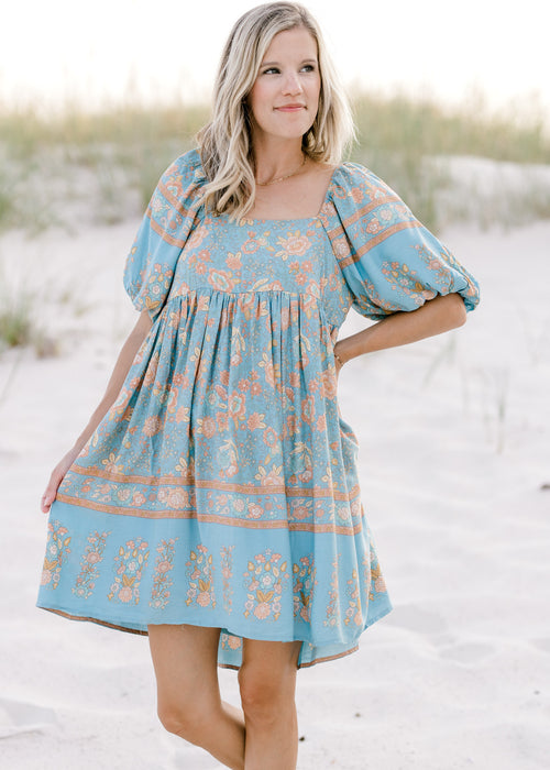 Model wearing a light blue dress with a gold floral pattern, square neck and bubble short sleeves.