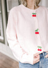 Model wearing a polyester pink cardigan with three cherry beaded clasp closure and long sleeves.