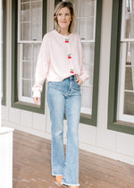 Model wearing jeans and a pink cardigan with three cherry beaded clasp closure and long sleeves.