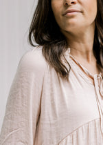 Close up of v-neck with a tie on a model in a blush top with a babydoll fit and long sleeves. 