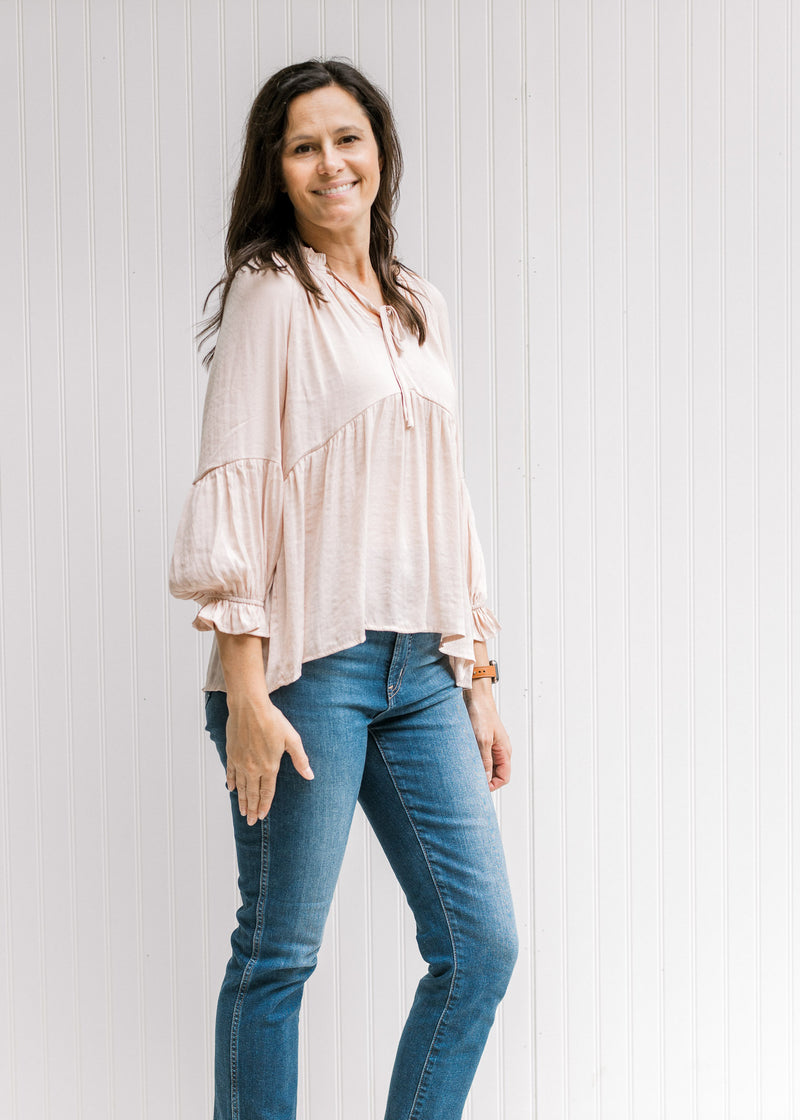 Model wearing jeans with a light pink v-neck top with a babydoll fit and long sleeves with a cuff. 