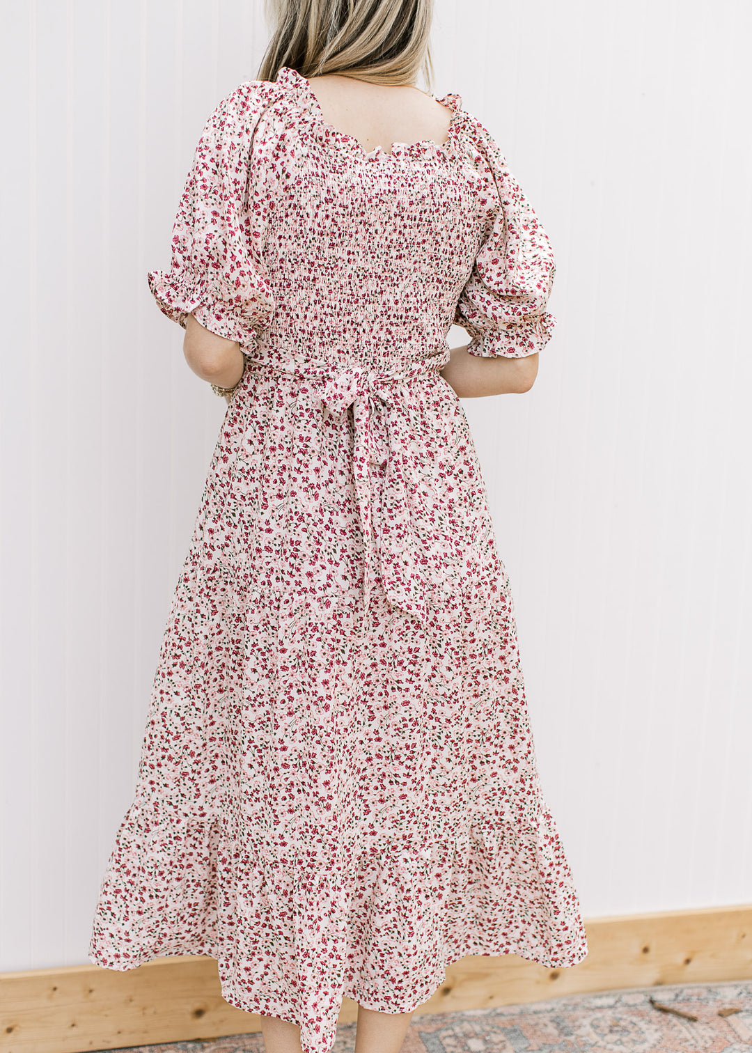 Back view of Model wearing a cream midi with floral, smocked bodice, tie back and short sleeves.