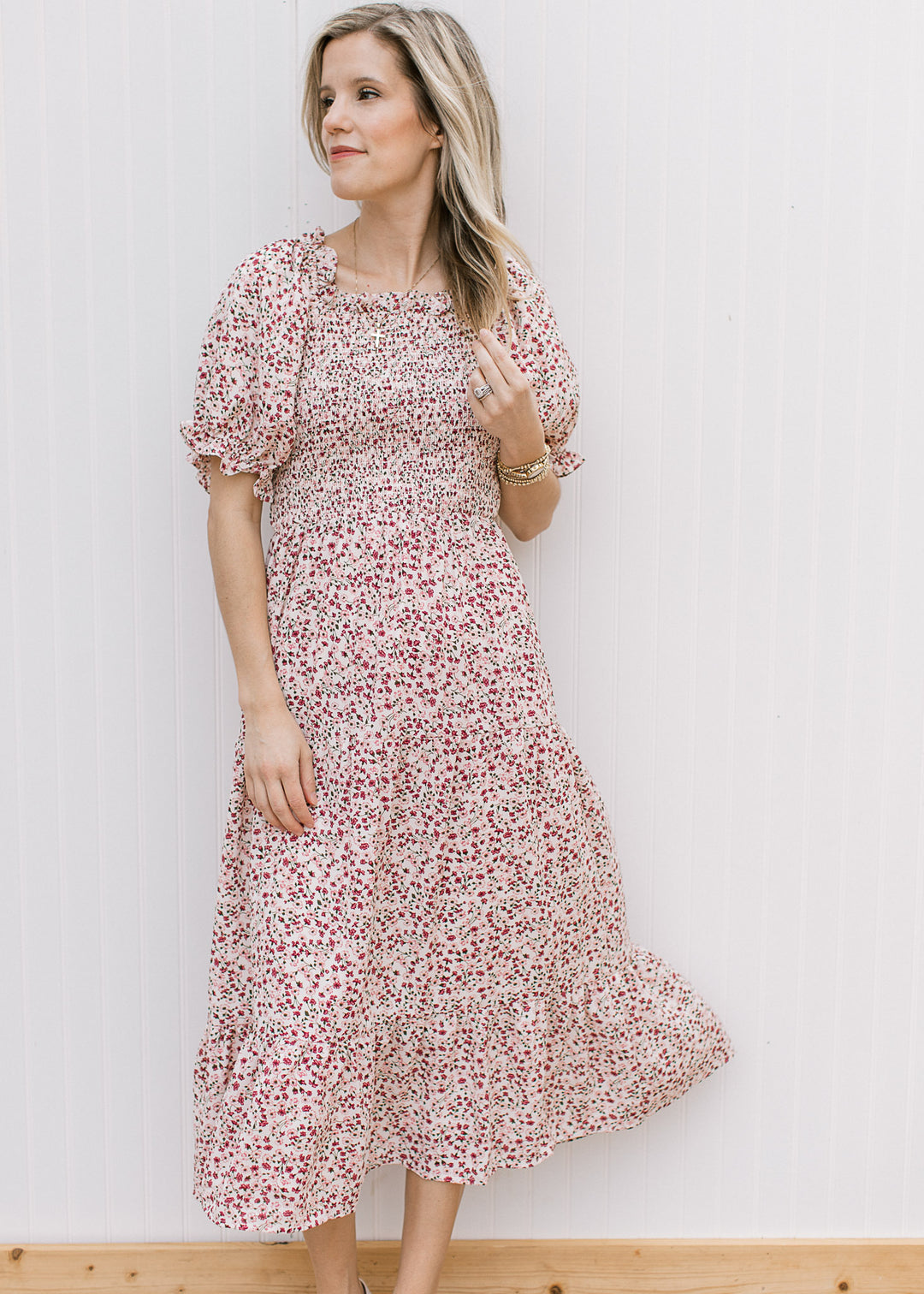 Model wearing a flowy cream midi with maroon and pink floral, smocked bodice and square neck. 