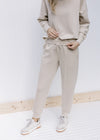 Model wearing sneakers and neutral colored joggers with cuffed ankles and a tie inside the waist.
