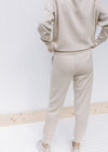 Back view of Model wearing neutral colored joggers with pockets, cuffed ankles and a tie at waist. 