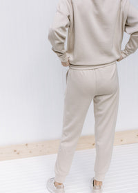 Back view of Model wearing neutral colored joggers with pockets, cuffed ankles and a tie at waist. 