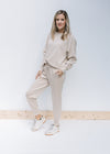 Model wearing sneakers with neutral colored sweatshirt and matching joggers with pockets. 
