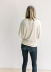 Back view of Model wearing a cream sweater with batwing sleeves, round neck and polyester material.