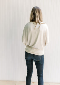 Back view of Model wearing a cream sweater with batwing sleeves, round neck and polyester material.