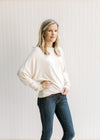 Model wearing a cream sweater with batwing long sleeves, round neck and polyester material. 
