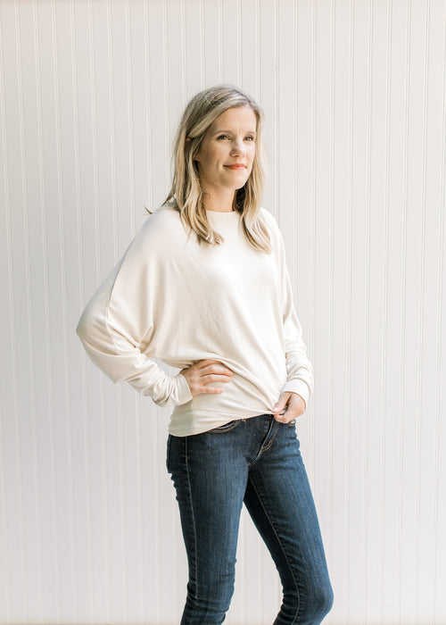 Model wearing a cream sweater with batwing long sleeves, round neck and polyester material. 