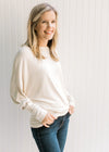 Model wearing jeans with a cream sweater with batwing sleeves, round neck and polyester material. 
