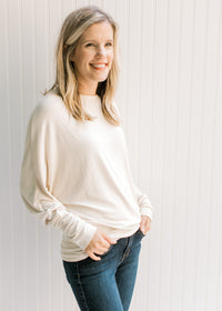 Model wearing jeans with a cream sweater with batwing sleeves, round neck and polyester material. 