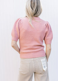 Back view of a short sleeve dusty blue sweater with pleated shoulders and ribbed detail. 
