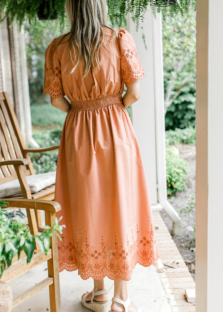 Back view of Model wearing a warm rust midi with eyelets, short sleeves, v-neck and tie front. 