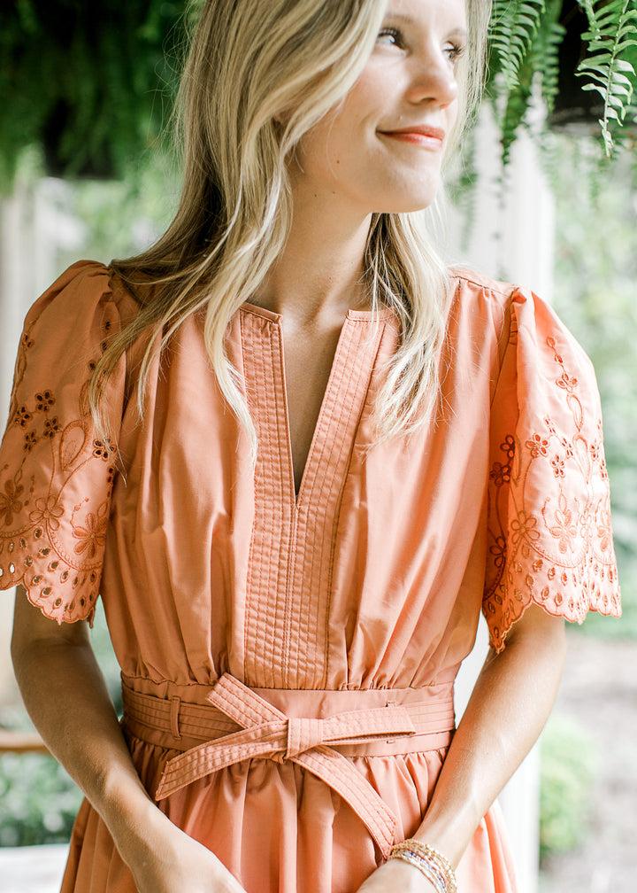 Model wearing a warm rust midi with a v-neck, tie at waist and short sleeves with scallops. 