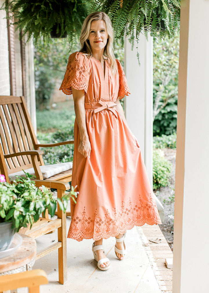 Model wearing a warm rust midi with tone on tone eyelets, short sleeves, v-neck and tie front. 