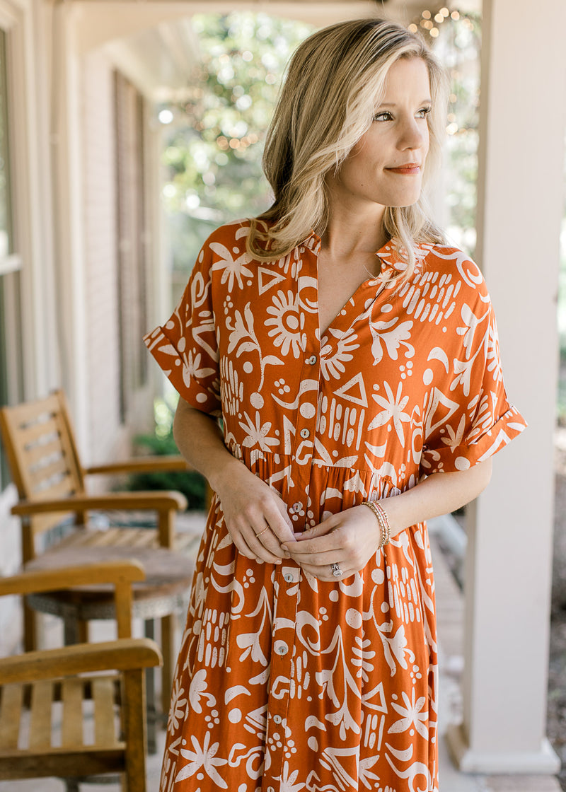Model wearing an orange button up midi with a cream print and short sleeves with cuffs.