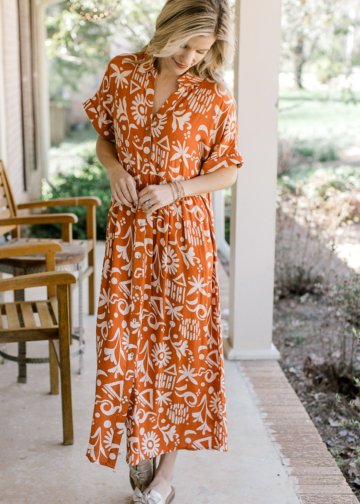 Model wearing sandals and an orange button up midi with a cream print and short sleeves with cuffs.