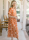 Side view of Model wearing an orange button up midi with a cream print and short sleeves with cuffs.