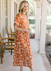 Side view of Model wearing an orange button up midi with a cream print and short sleeves with cuffs.