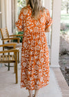 Back view of Model wearing an orange button up midi with a cream print and short sleeves with cuffs.