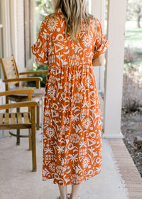 Back view of Model wearing an orange button up midi with a cream print and short sleeves with cuffs.